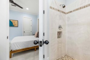 A bedroom with a bed, a door, and a shower area with tiled walls and a showerhead. - Luxe, Lakefront, Heated Pool/Spa, 5 mins to Beach (Santa Rosa Beach)