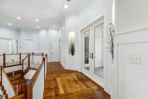 A spacious hallway with wooden flooring, white walls, and a wooden staircase with white railings.