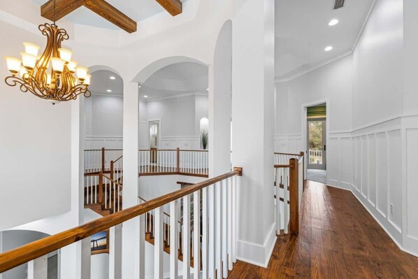 A spacious interior with a wooden staircase, white walls, and a chandelier.