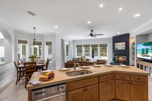 Una cocina amplia con una isla central, un comedor con sillas de madera, una sala de estar con sofá y televisión, y una chimenea.
