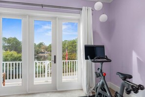 A room with a large sliding glass door leading to a balcony, a stationary exercise bike, and a small TV mounted on the wall.