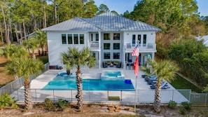 A two-story house with a large swimming pool, outdoor seating, and a flag. - Luxe, Lakefront, Heated Pool/Spa, 5 mins to Beach (Santa Rosa Beach)