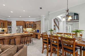 A spacious kitchen with wooden cabinets, a central island with stools, and a dining area with a large wooden table and chairs. - Luxe, Lakefront, Heated Pool/Spa, 5 mins to Beach (Santa Rosa Beach)
