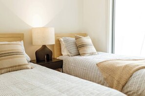 A hotel room with two beds, a nightstand with a lamp, and a window providing natural light. - Waterfront at Serenity (Maroochydore)