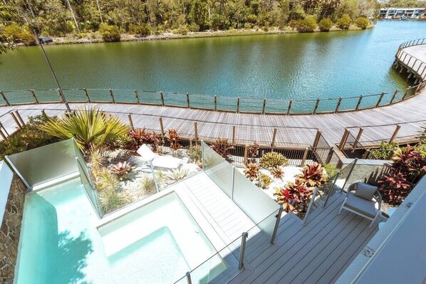 A rooftop pool with a glass balustrade, surrounded by tropical plants and a wooden deck.