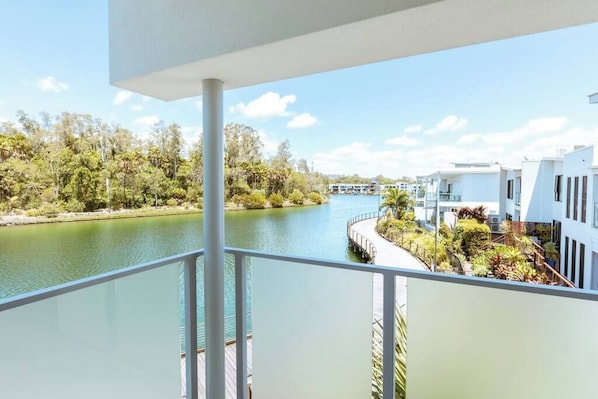 Un balcon donnant sur une rivière, entouré de verdure et de bâtiments modernes.