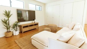 A modern living room with a sofa, a TV, a wooden cabinet, and a ceiling fan. - Waterfront at Serenity (Maroochydore)
