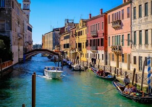 Un canal de Venise, avec des gondoles, un pont et des bâtiments aux couleurs vives.
