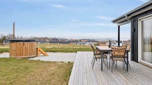 Eine Holzterrasse mit Whirlpool, Sitzgelegenheiten im Freien und Blick auf die Landschaft.