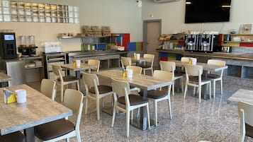 Un caffè moderno con numerosi tavoli e sedie, un angolo caffetteria e una televisione a parete.