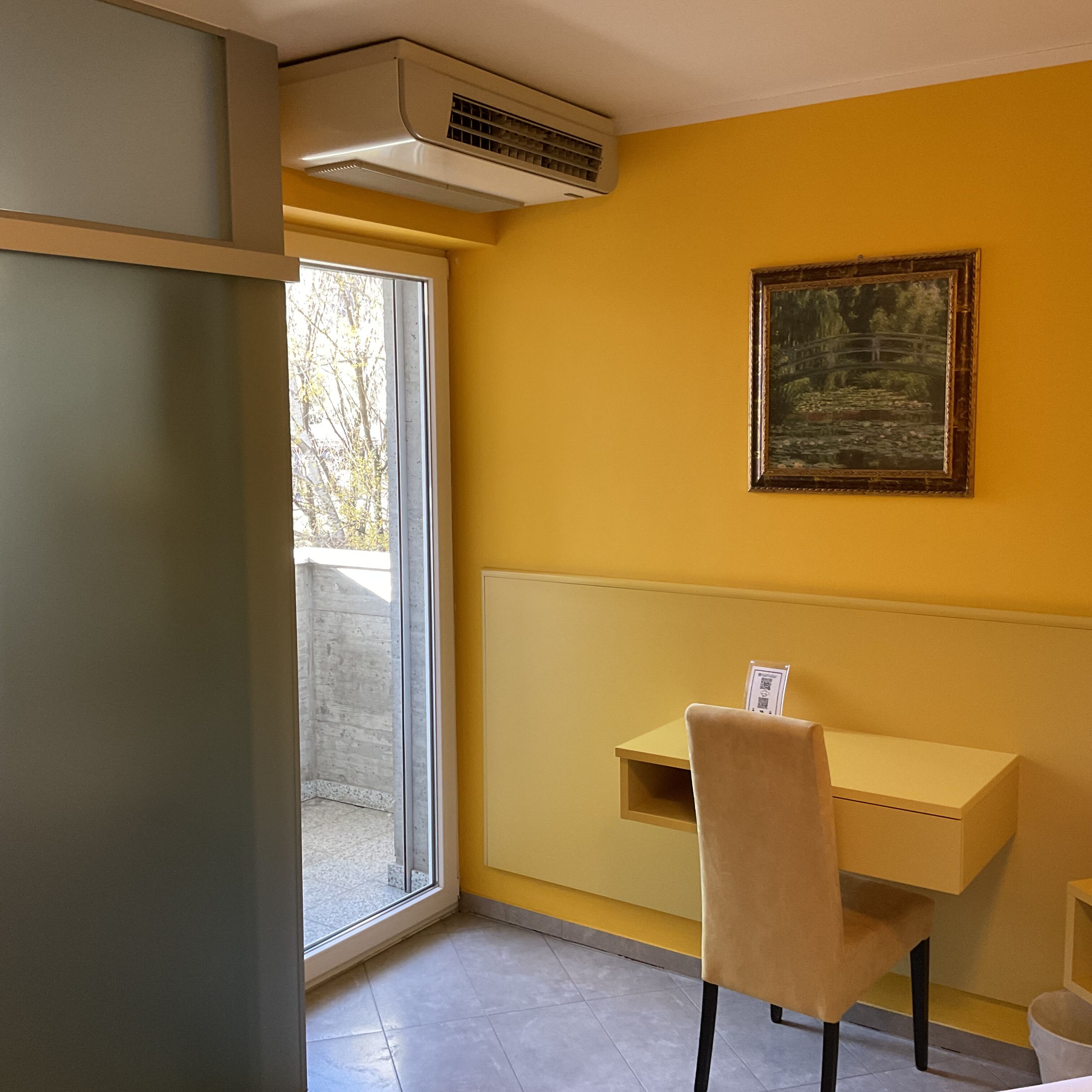 Une pièce avec un mur jaune, un tableau, une fenêtre, une table et une chaise.