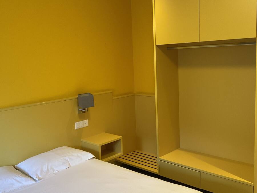 Camera d'albergo con un letto, un armadio, un comodino e una lampada a muro.