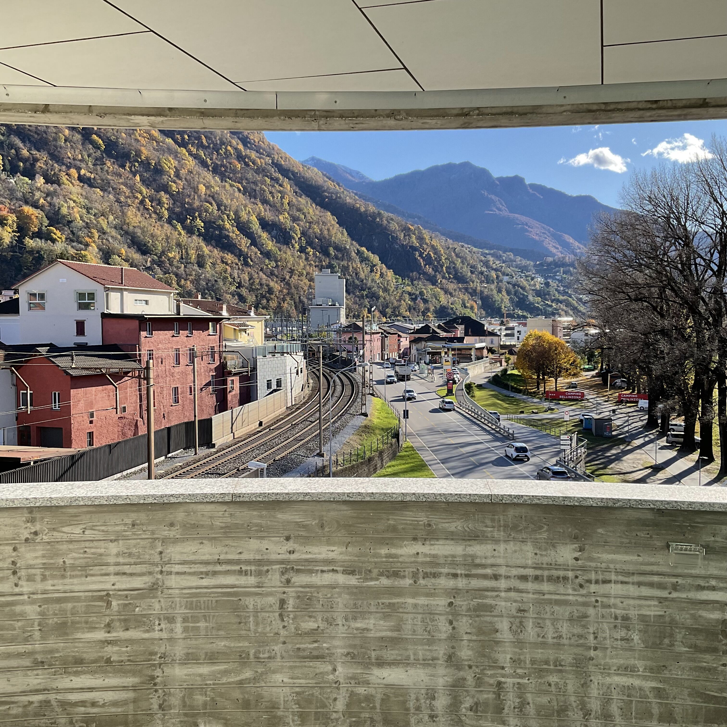 A view of a train station with tracks, a road, and buildings in the background.