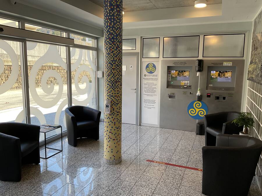 A hotel lobby with a check-in/check-out kiosk, seating area, and a decorative pillar.
