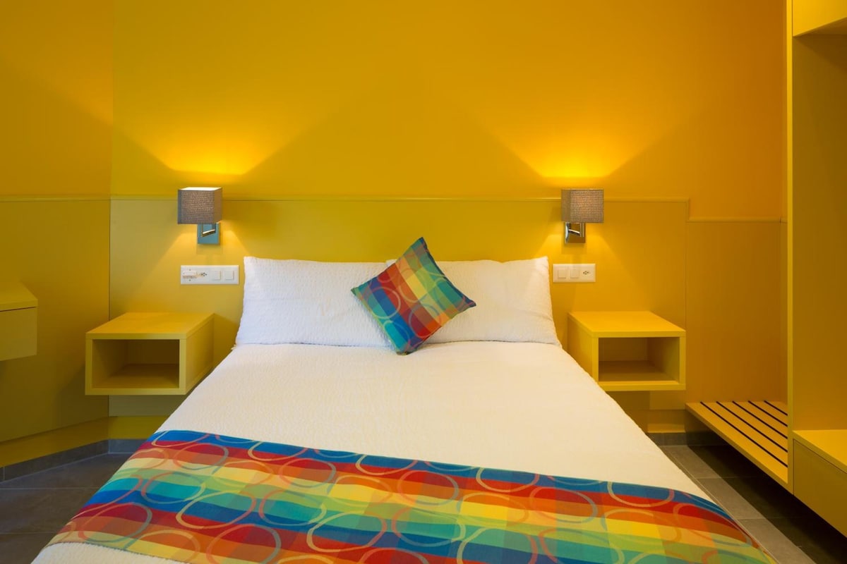 A hotel room with a large bed, two bedside tables, and two wall-mounted lamps.