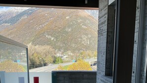 A balcony with a view of a mountainous landscape, a glass door with a red 'H' sign, and a tiled floor. - Hotel Liberty Self Check-in (Bellinzona)