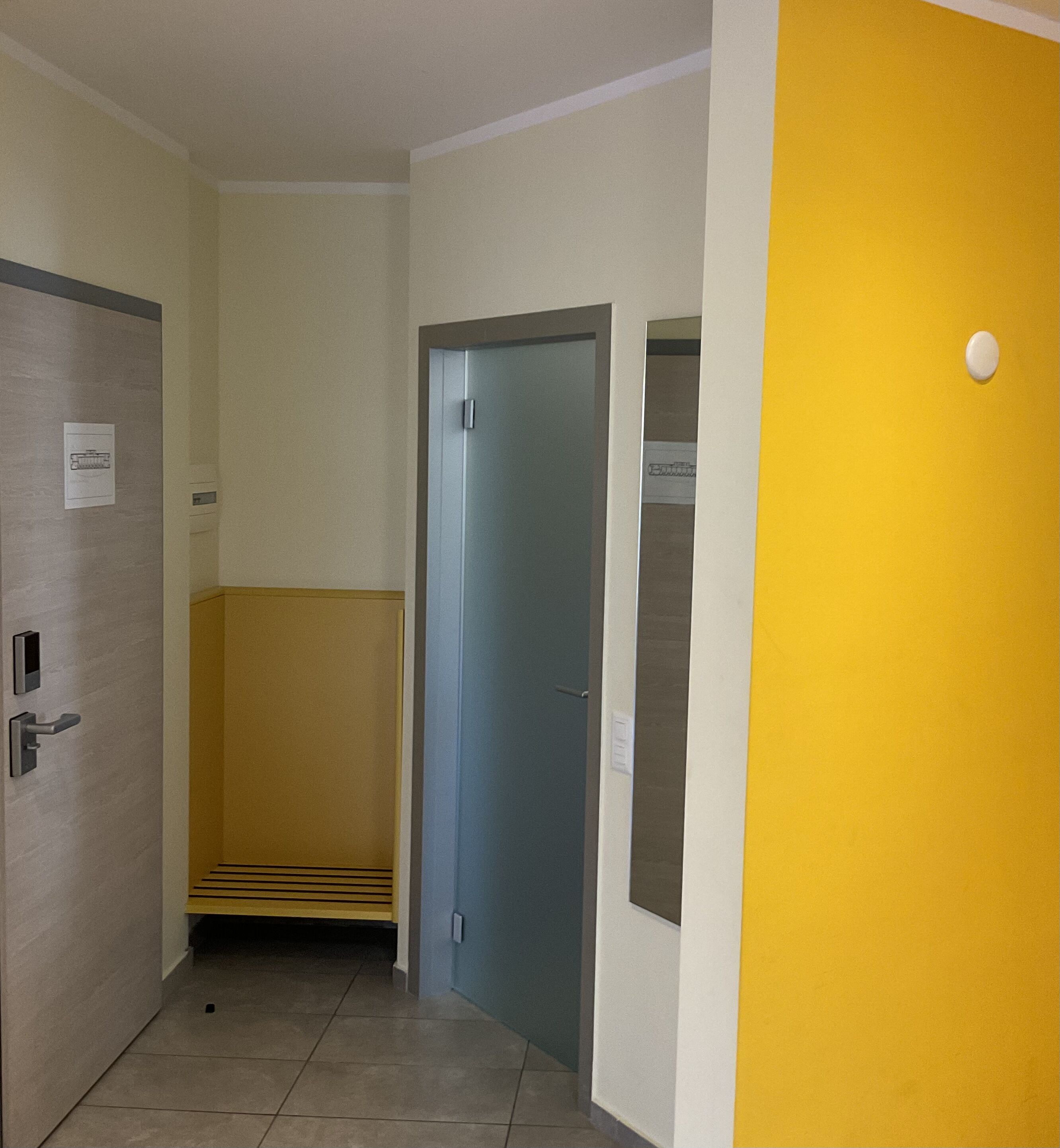 Un pasillo con una puerta a la izquierda, una puerta azul en el centro y una pared amarilla a la derecha.