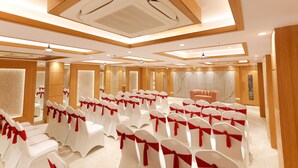 A conference room with rows of white chairs with red sashes, wooden paneling, and a marble wall. - Hotel Sarc Inn (Varanasi)