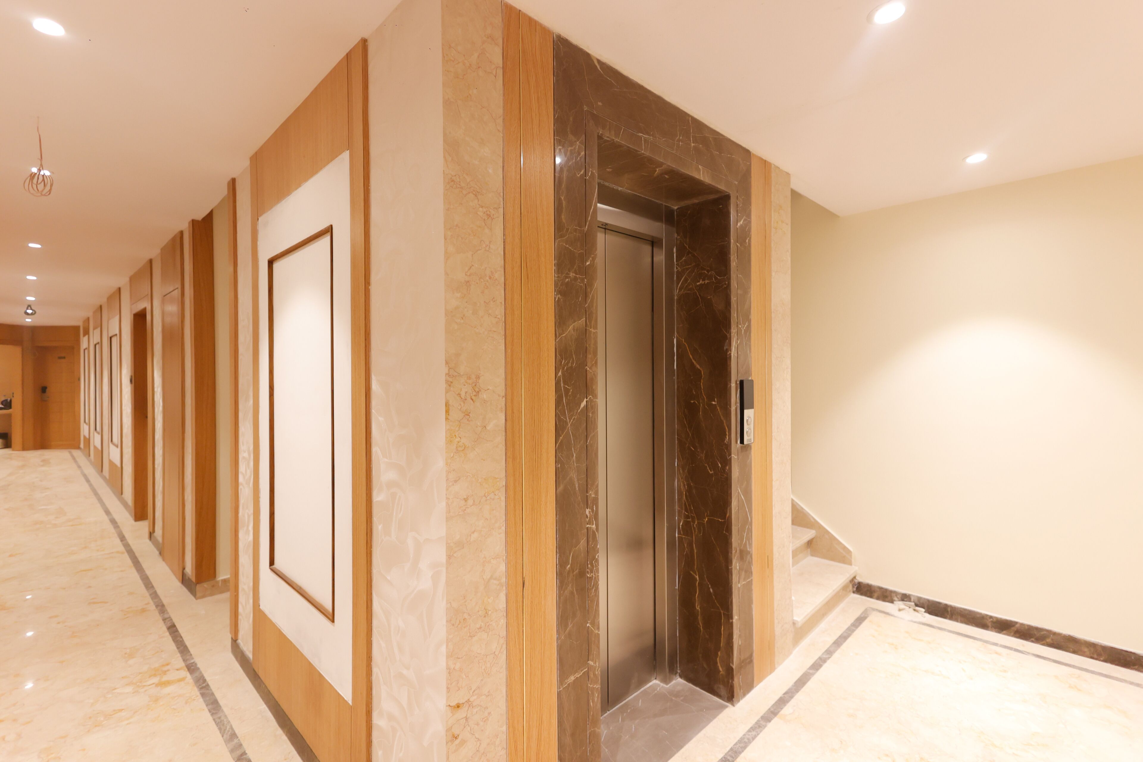 A hotel corridor with a marble floor, wooden paneling, and an elevator.