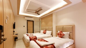 A hotel room with two beds, a ceiling fan, an air conditioning unit, and a wooden wardrobe. - Hotel Sarc Inn (Varanasi)