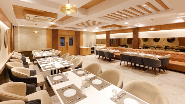 A modern dining area with multiple tables and chairs, a long counter with a bar, and a seating area with a sofa. - Hotel Sarc Inn (Varanasi)