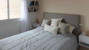 Un lit bien fait, avec une couette matelassée, une table de chevet avec une lampe et une bibliothèque adossée au mur.