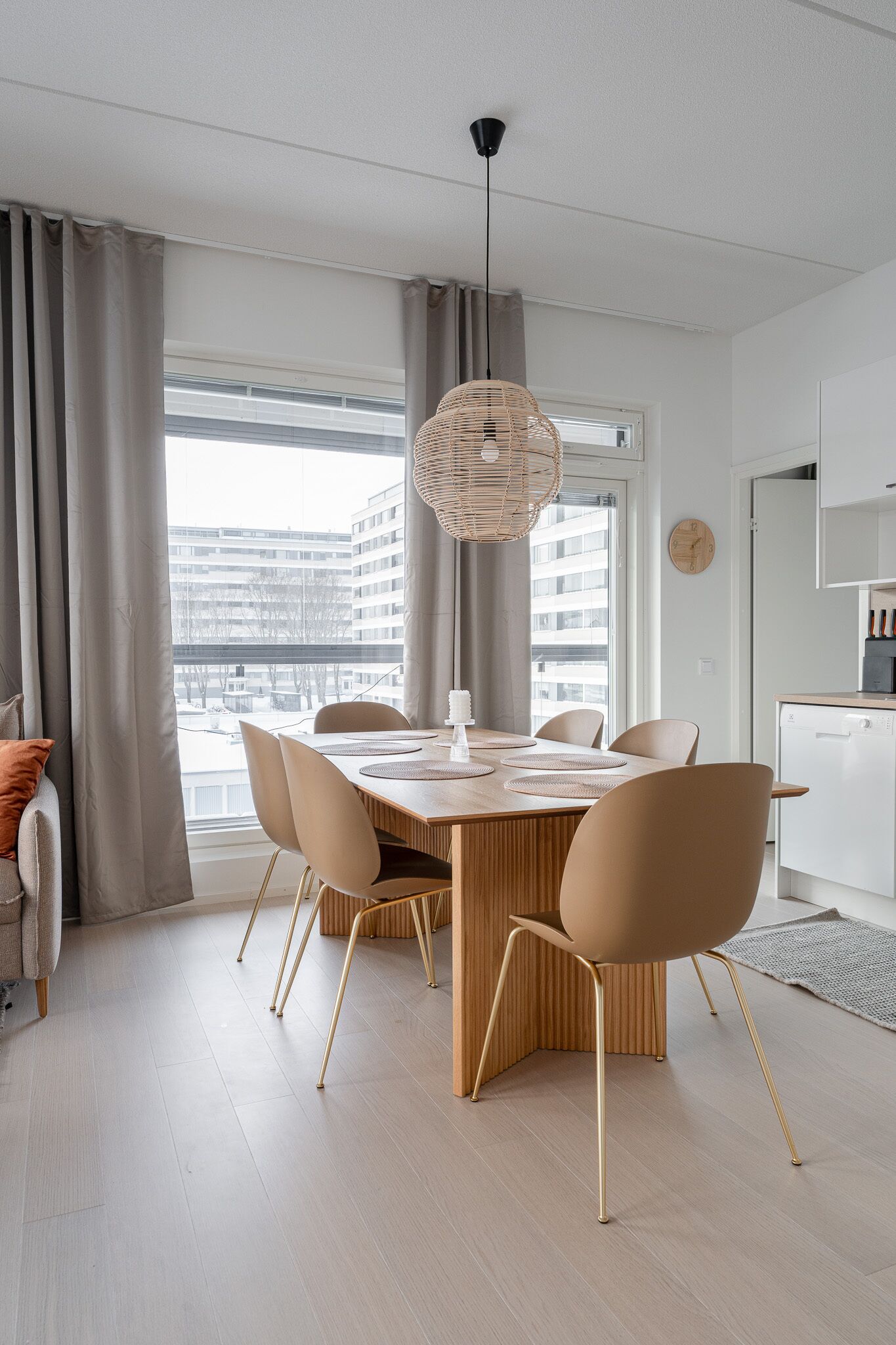 A modern dining area with a wooden table, beige chairs, and a woven pendant light.