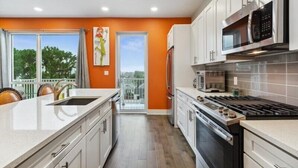 Una cocina moderna con armarios blancos, una estufa de acero inoxidable y un amplio ventanal con vistas a un balcón.