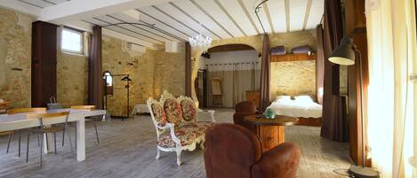 Une pièce spacieuse avec un plafond haut, des murs en pierre, un plancher en bois, un grand lit, une table à manger avec des chaises et un lustre.