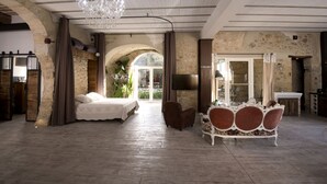 A spacious room with a large bed, a chandelier, a TV, and a dining area with a table and chairs. - Gites la Remise (PUIMISSON)