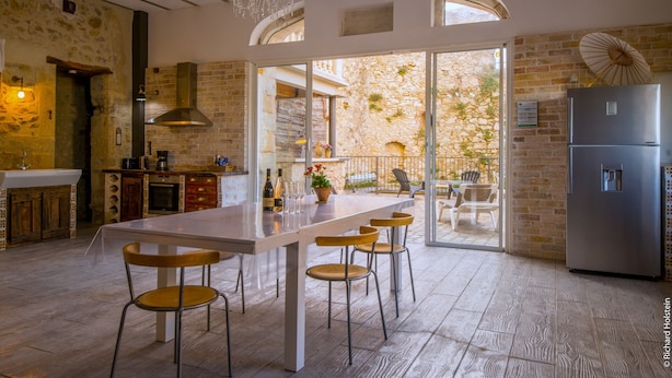 A kitchen with a central island, bar stools, a chandelier, and a view of the outdoor patio. - Gites la Remise (PUIMISSON)