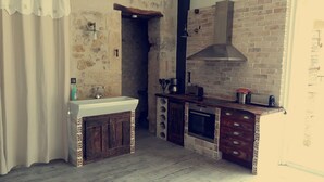 A rustic kitchen with a stone wall, wooden cabinets, and a built-in oven. - Gites la Remise (PUIMISSON)