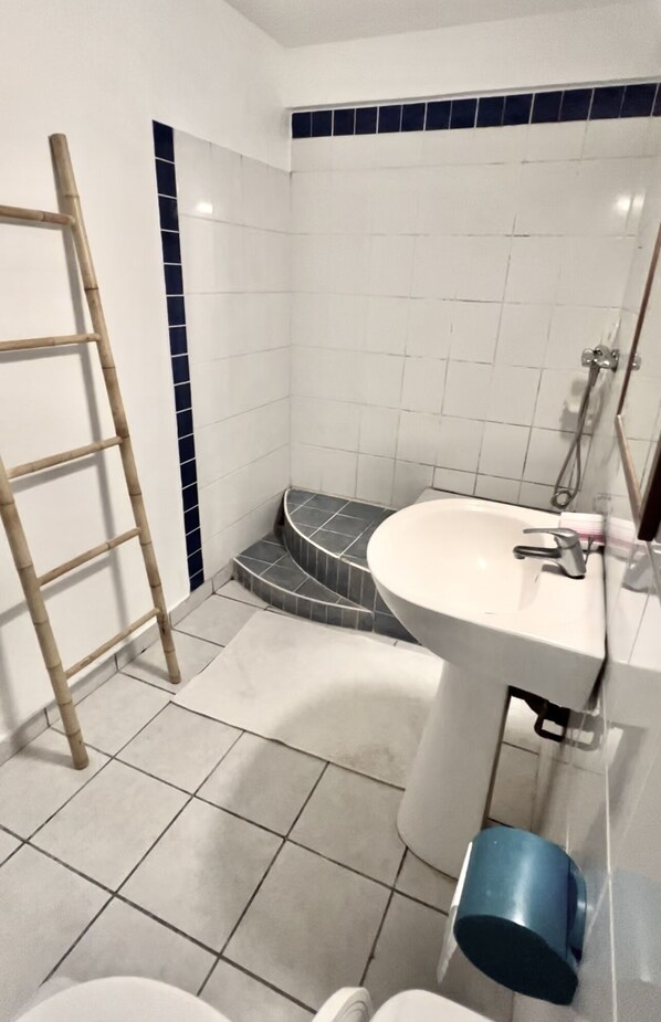Un baño con un lavabo blanco, un espejo, una ducha y una escalera de madera.