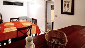 Un coin repas avec une table mise pour quatre personnes, un vase et un panier posés sur la table.