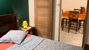Une chambre à coucher comprenant un lit, une table de chevet, une lampe, une armoire en bois et un coin repas avec une table et des chaises.