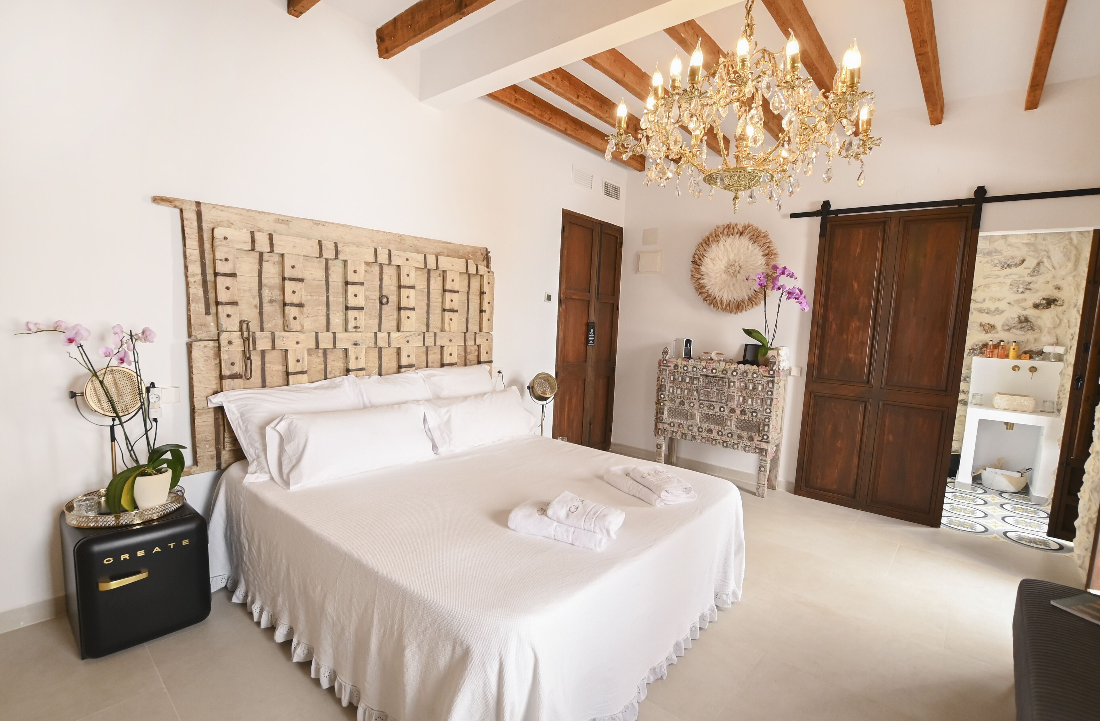 A bedroom with a large bed, a chandelier, a wooden headboard, and a dresser with a mirror.