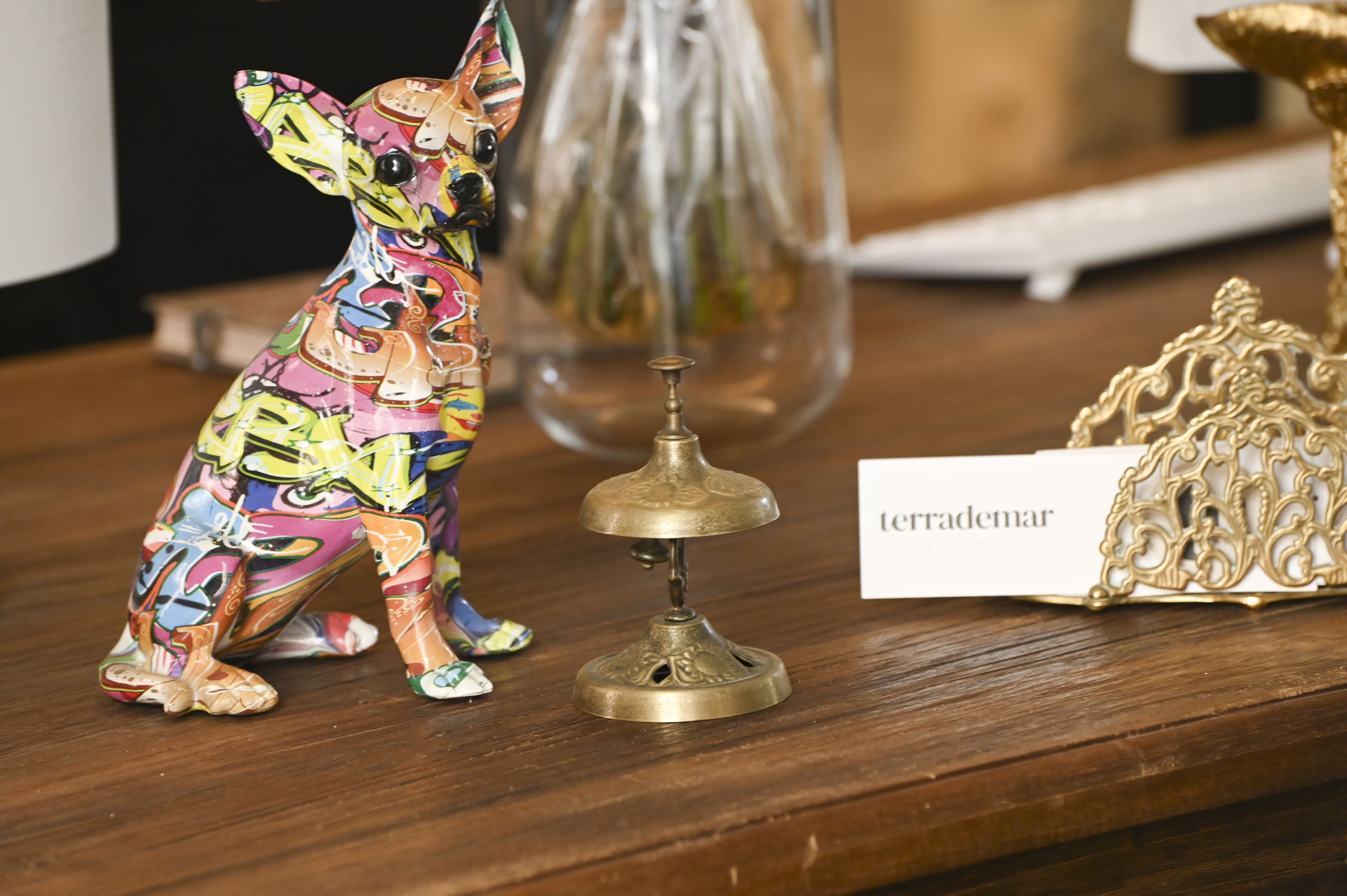 Una figurita de perro de colores, una campana de bronce y un adorno sobre una superficie de madera.