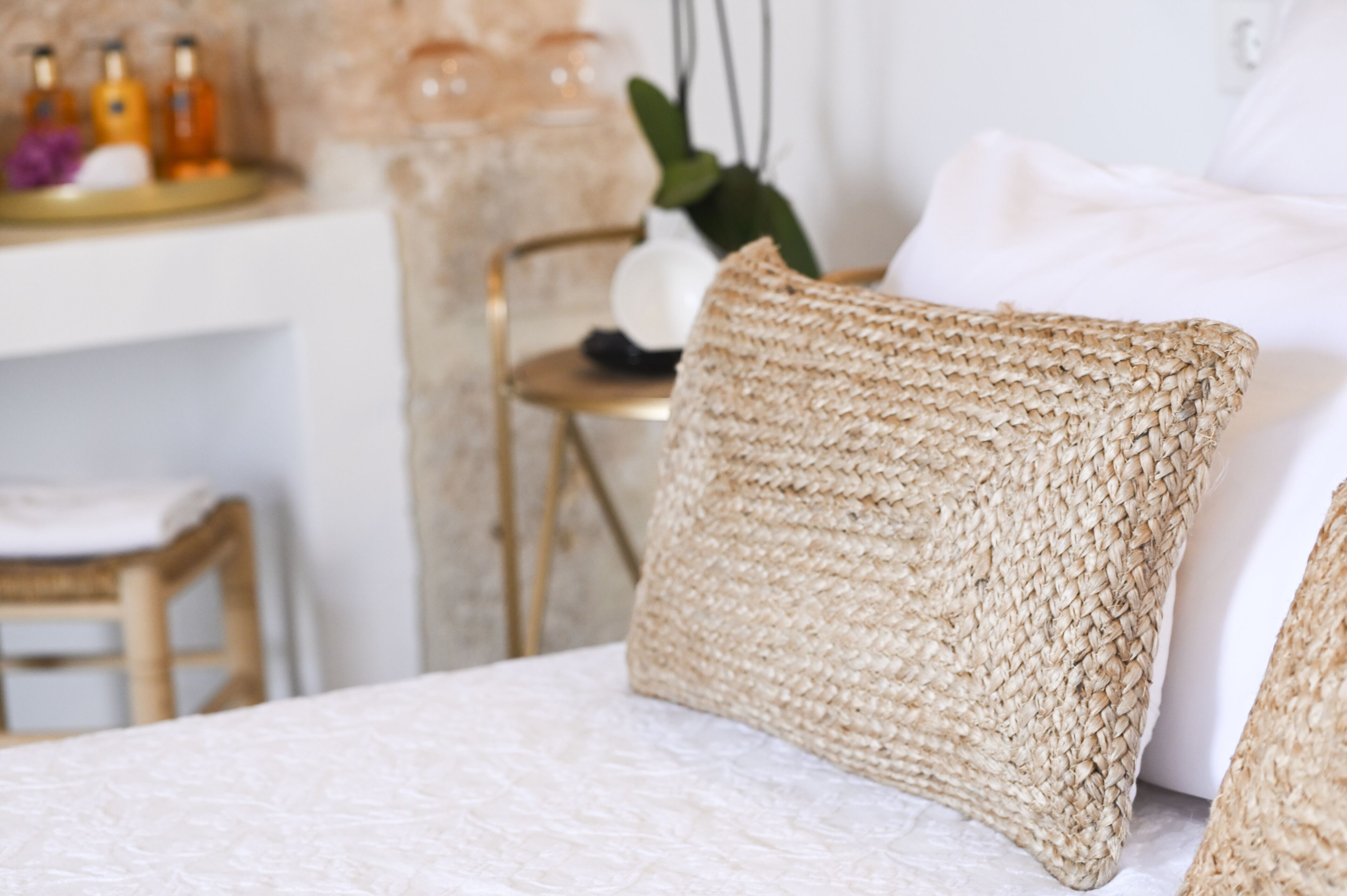 A bed with a woven pillow and a white textured bedspread.