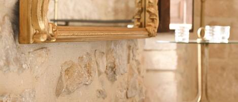 A gold-framed mirror on a marble wall with a glass table below.