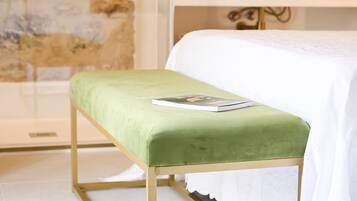 Una cama con una colcha blanca y un banco tapizado en verde con un libro encima.