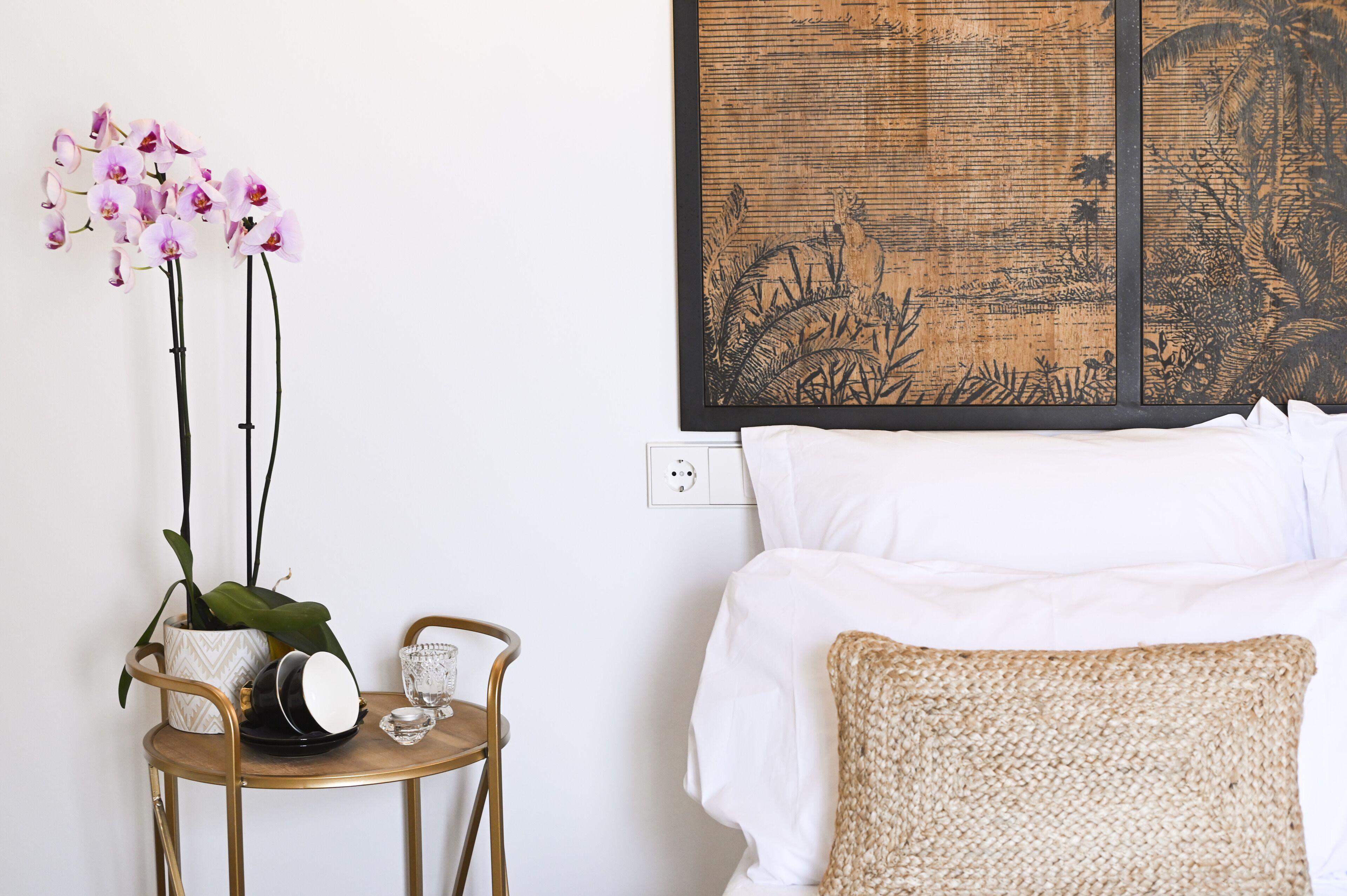 A hotel room with a bed, a wall-mounted artwork, a small table with a potted plant, and a chair.