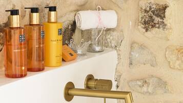 Un baño con lavamanos blanco, grifo dorado y artículos de aseo, incluyendo botellas de jabón para manos y cuerpo.