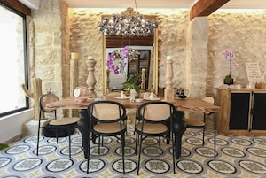 Uma sala de jantar com parede de pedra, um candelabro e uma mesa posta para seis.