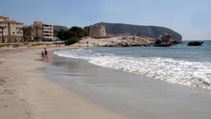 A beach with a castle-like structure, sandy shore, and clear blue sky. - Ca sana Boutique Taulada Moraira (Teulada)