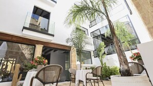 An outdoor patio with wicker chairs and a table, surrounded by potted plants and a palm tree. - Ca sana Boutique Taulada Moraira (Teulada)