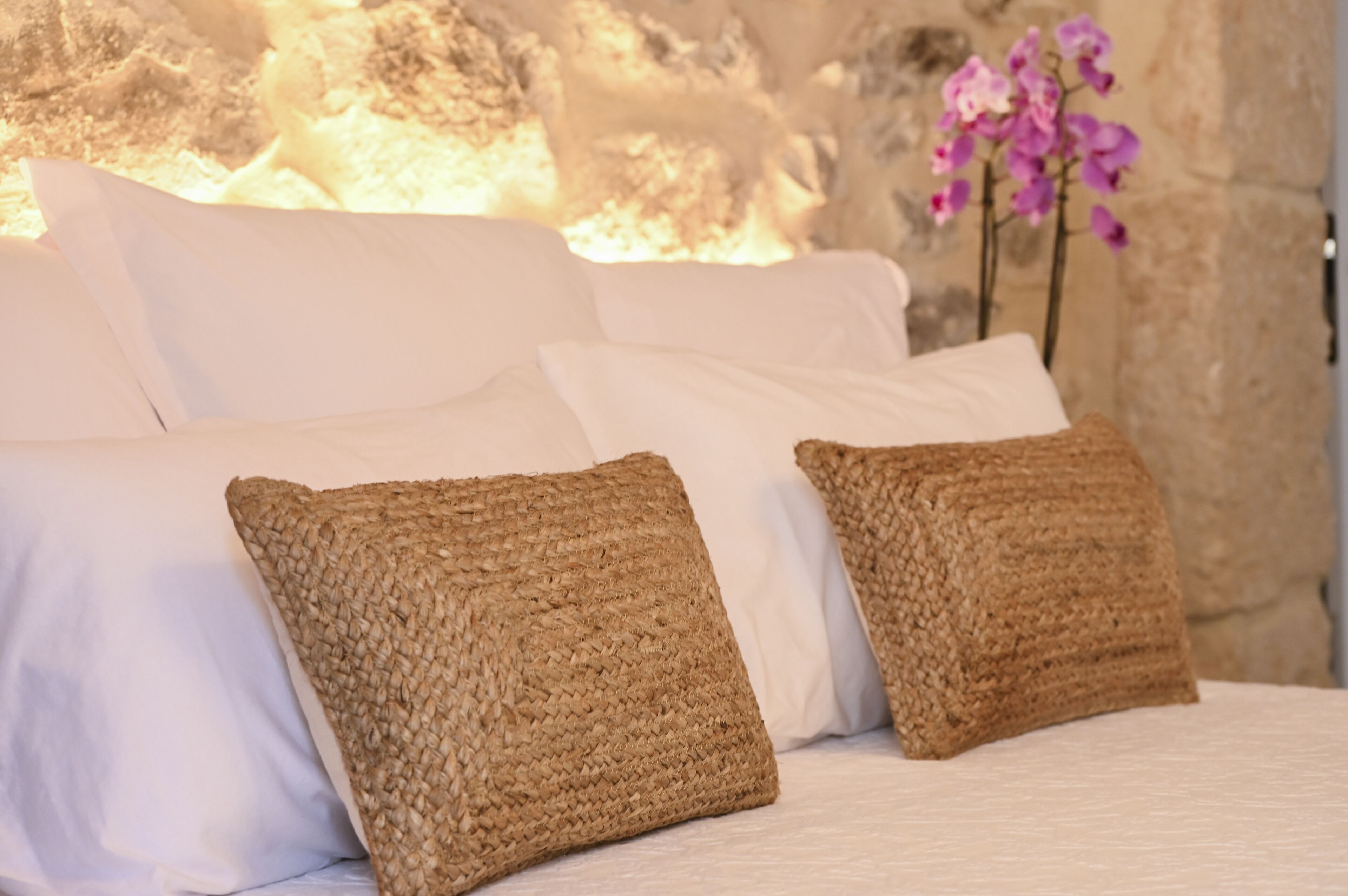 A bed with white linens and two woven brown pillows.