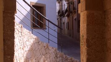 An arched stone entrance leading to a staircase with a metal handrail, surrounded by buildings with balconies.