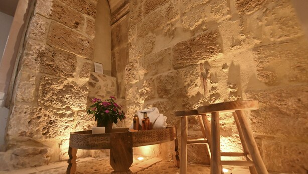 A stone-walled room with a wooden bench and a small table holding toiletries and a potted plant. - Ca sana Boutique Taulada Moraira (Teulada)