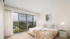 A hotel room with a large bed, a view through a sliding glass door, a painting on the wall, and a nightstand with a lamp. - Netflix，Peaceful 3BR Morningside Gem: Cozy Retreat (Morningside)