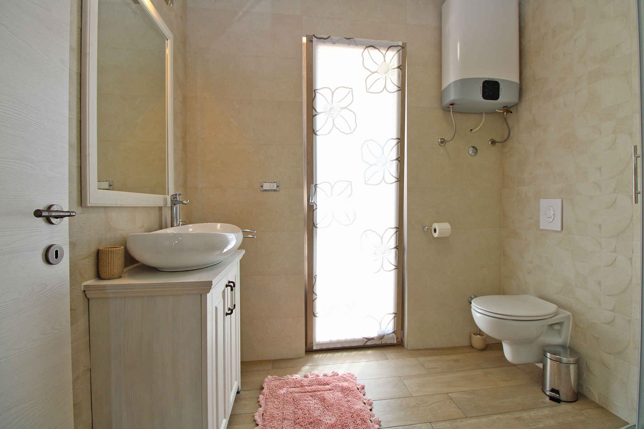 A bathroom with a sink, mirror, toilet, and a shower with a flower-patterned door.